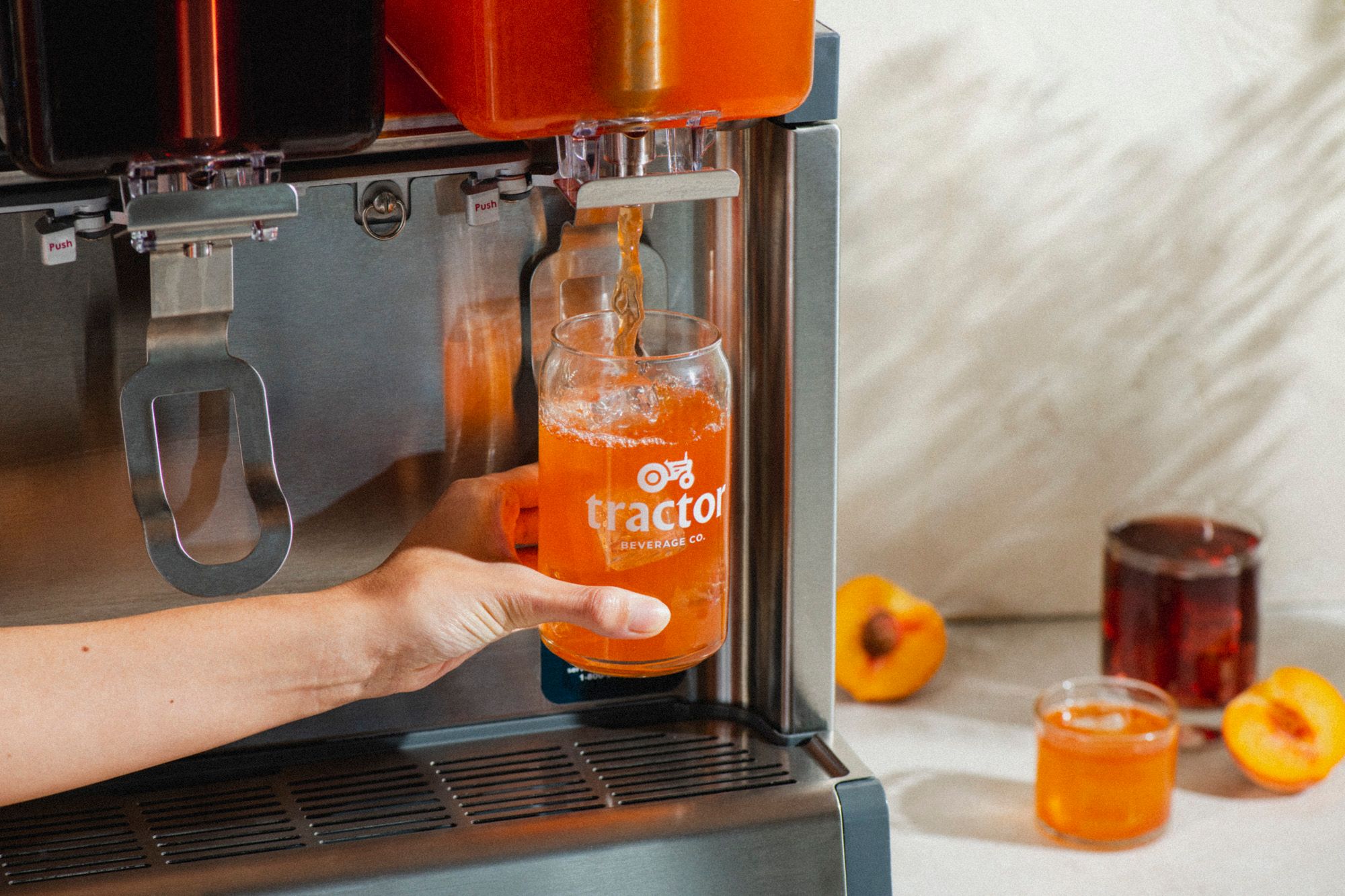 Person pouring an orange fountain drink in a glass that says Tractor Beverage Co.