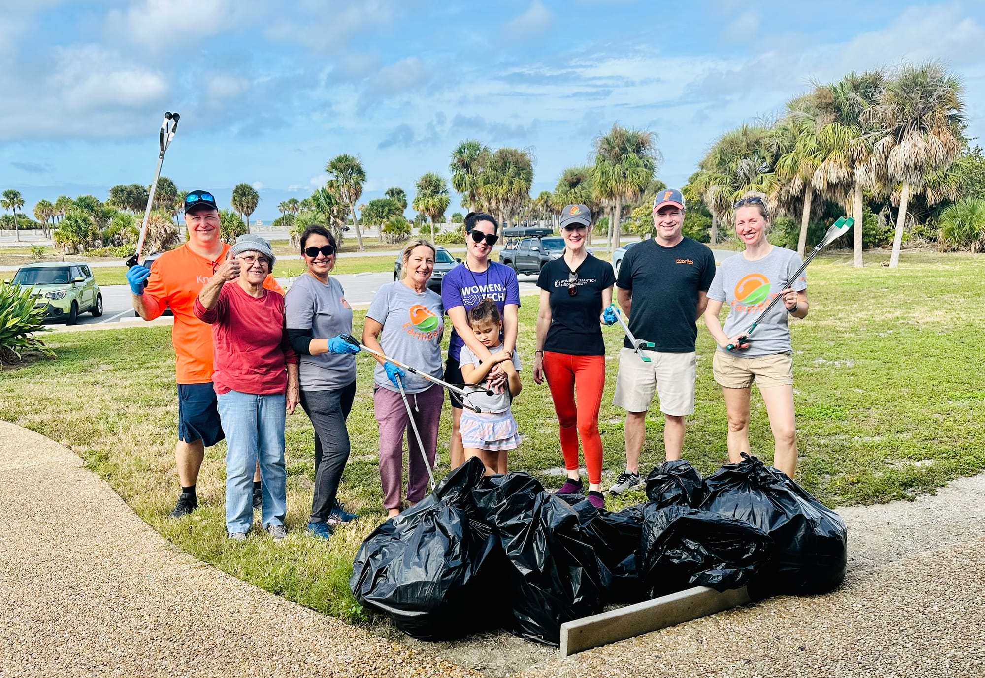Group of people at a cleanup event holding trash pickers and posing in front of trash bags