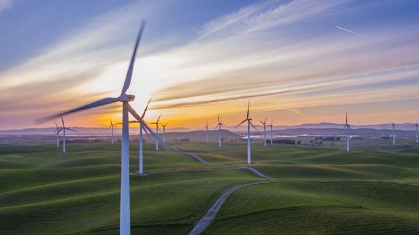 Windmills on small, rolling green hills in front of a sunset